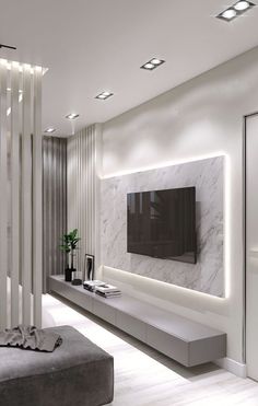 a modern living room with white walls and marble furniture, along with a large flat screen tv mounted on the wall