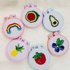 four cross stitch hoop holders with fruit and vegetables in them on a white tablecloth