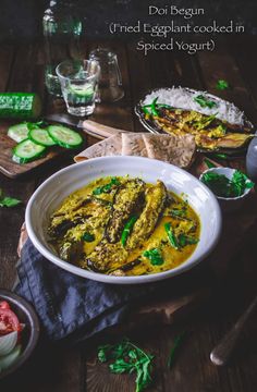 a white bowl filled with food sitting on top of a wooden table next to cucumbers