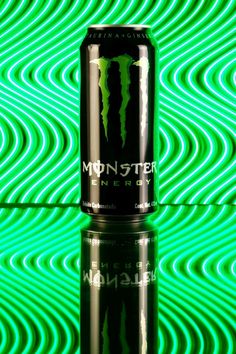 a can of monster energy drink sitting on top of a green and black background with wavy lines