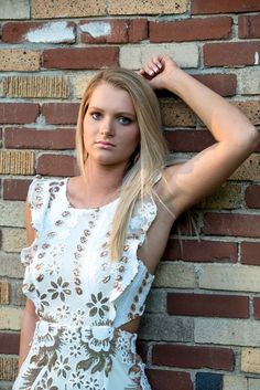 a beautiful blonde woman leaning against a brick wall