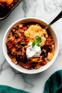 a bowl of chili with sour cream and tortilla bread in it on a marble table