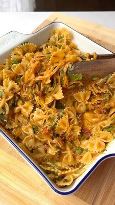 a wooden spoon is in a white bowl filled with pasta and sauce on a cutting board