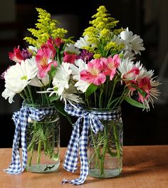 two mason jars filled with colorful flowers sitting on a wooden table next to each other