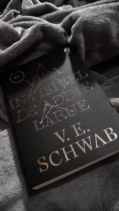 a book laying on top of a bed covered in gray sheets and blankets with writing on the cover