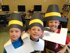 three children wearing paper hats and holding up signs in front of their faces with computers on the desk behind them