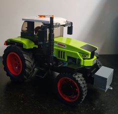 a green toy tractor with red wheels on a black surface