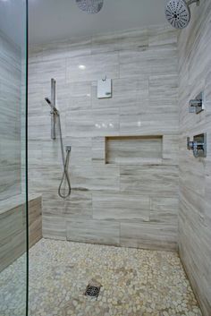 a walk in shower sitting next to a glass door and tiled walls with pebbles on the floor