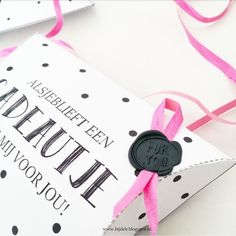 a pink ribbon is tied around the top of a white box with a black stamp on it