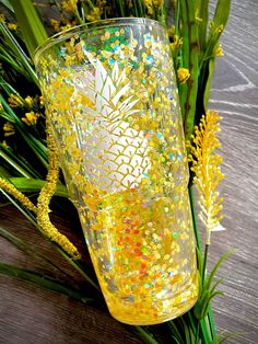 a pineapple glass sitting on top of a wooden table next to some yellow flowers