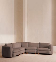 a living room with a large sectional couch and wooden legs on the floor in front of a white wall