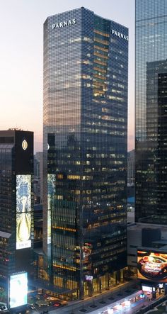 an aerial view of some very tall buildings in the city at night with traffic passing by