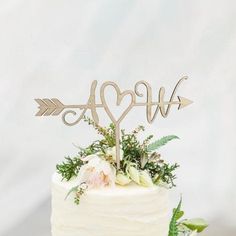 a wedding cake with an arrow topper and greenery on the side, sitting on a table