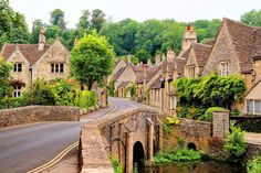 an old stone bridge over a river in the middle of a village with houses on either side