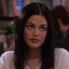 a woman with long black hair sitting in front of a bookshelf and looking at the camera