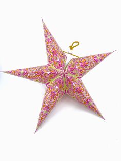 an origami star is hanging from a string on a white background with pink and yellow designs