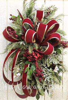 a christmas wreath hanging on the side of a building with red ribbon and greenery