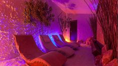 the room is lit up with purple lights and pillows on the floor, along with plants