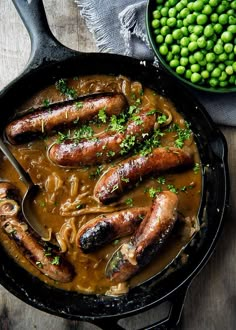 some sausages are in a brown gravy next to peas