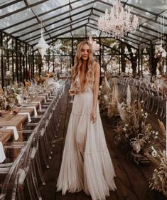 a woman in a white dress standing next to a long table with chairs and chandeliers