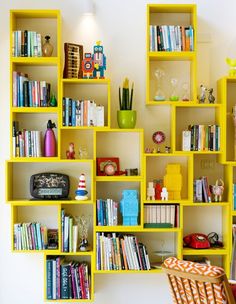 a yellow book shelf filled with lots of books next to a table and chair in front of a white wall