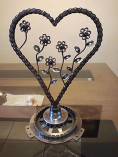 a metal sculpture with flowers in the shape of a heart on top of a table