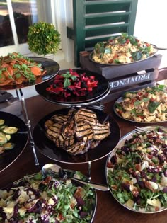 a table topped with lots of different types of plates filled with salads and meat