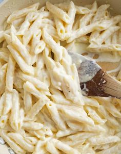 a wooden spoon in a bowl filled with macaroni and cheese pasta on a table