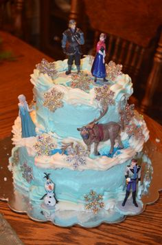 there is a blue cake with figurines on it and snowmen in the background