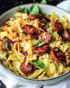 a bowl filled with pasta and sausages on top of a white table cloth next to a fork