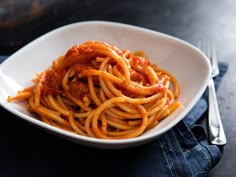 a white bowl filled with spaghetti on top of a blue cloth next to a fork