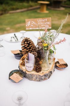 a table topped with pine cones and vases on top of a white table cloth