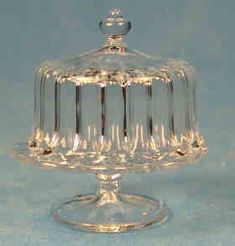 a clear glass cake dish with a domed top on a blue tableclothed background