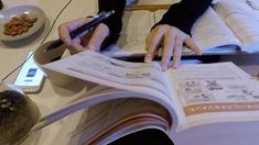 a person sitting at a table with an open book in front of them and holding a pen