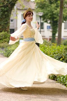 a woman in a long white dress and hat is walking down the street with her arms outstretched