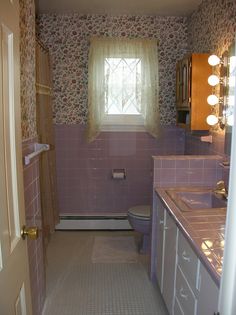 a bathroom with pink tile and floral wallpaper is seen through the doorway to another room