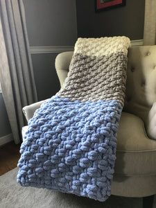 a blue and white crocheted blanket sitting on top of a chair next to a window