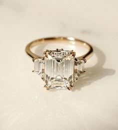 an emerald cut diamond ring on a white surface