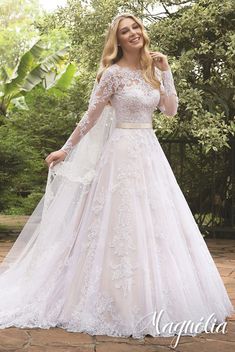 a woman in a white wedding dress standing on a brick walkway with trees and bushes behind her