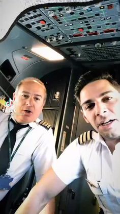 two pilots in the cockpit of an airplane, one is talking on his cell phone