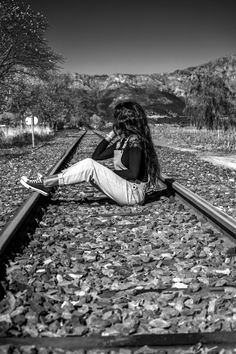 a woman sitting on the railroad tracks with her legs crossed, looking at something in the distance