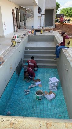 two men sitting on the ground in front of a building under construction with blue tiles