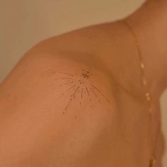 the back of a woman's shoulder with small stars on it and a starburst tattoo