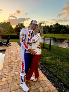 a man and woman standing next to each other in front of a lake at sunset