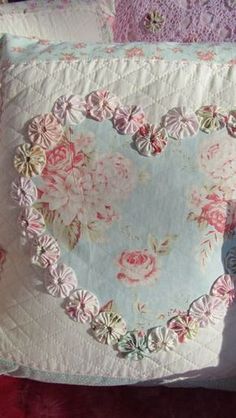 a heart shaped pillow on top of a pink and purple bed sheet with flowers in the middle