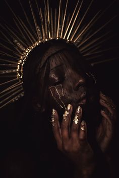 a woman with her hands on her face and gold painted nails covering her face, in the dark