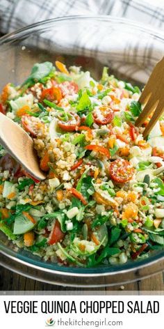 vegetable quinoa chopped salad in a glass bowl with a wooden spoon on the side