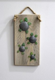 a wooden plaque with seashells and green leaves on it hanging from a rope