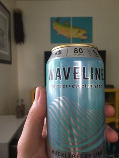 a person holding up a can of waveline beer in front of a television set