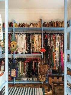 an organized closet with clothes and handbags hanging on the shelves, in front of a striped rug